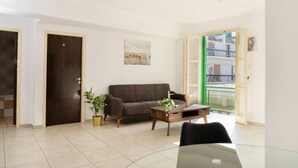 Un salon avec un canapé, une table basse, une plante en pot et une vue sur l’extérieur, visible à travers une porte.