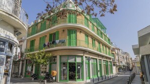 Un immeuble à plusieurs étages doté d’une façade incurvée, de volets verts et d’un commerce visible au rez-de-chaussée.