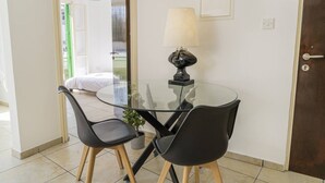 Une petite pièce avec une table en verre, deux chaises, une lampe et une porte.