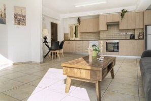 Ein modernes Wohnzimmer mit Couchtisch aus Holz, einem Essbereich mit schwarzen Stühlen und einer Küche mit Holzschränken und fest eingebautem Backofen.