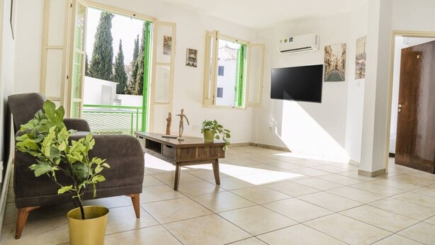 Un salon avec un canapé, une table basse, une plante en pot, un téléviseur et une porte.