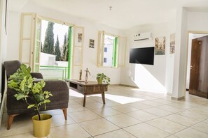 Ein Wohnzimmer mit einer Couch, einem Couchtisch, einer Zimmerpflanze, einem Fernseher und einer Tür.