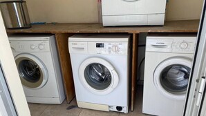 Un cuarto de lavandería con tres lavadoras, un estante con un recipiente metálico y una encimera de madera.