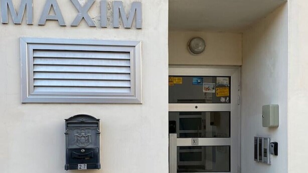 Entrada de un edificio con el nombre 'MAXIM' sobre un buzón y una puerta con un panel de vidrio.