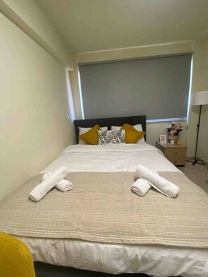 A neatly made bed with white linens and two rolled towels, a bedside table with a lamp, and a window with a view. - Modern studio in historic center, near beach, view (Limassol)