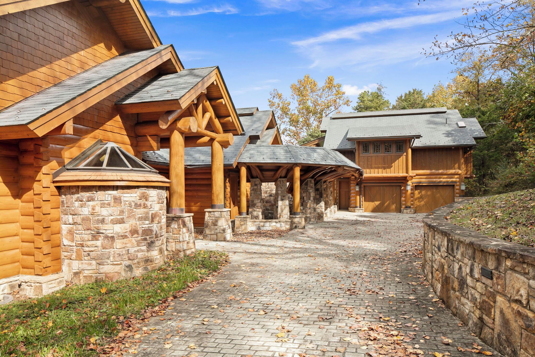 A log cabin with a stone foundation, a covered outdoor area, and a brick pathway.