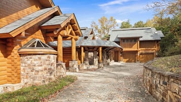 A log cabin with a stone foundation, a covered outdoor area, and a brick pathway.