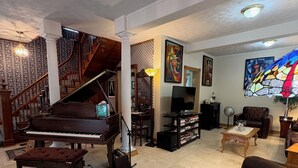 Un ampio soggiorno con un pianoforte a coda, un divano confortevole, una scala con ringhiere elaborate e un'ampia finestra a vetri colorati.