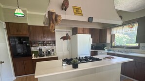 Una cucina con mobili in legno, un'isola bianca, un frigorifero e un cartello che avverte della presenza di uomini al lavoro in cucina.
