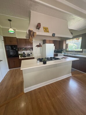 Eine Küche mit Holzausstattung, einer weißen Kochinsel, einem Kühlschrank und einem Schild mit der Warnung, dass dort Männer kochen.