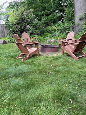 Ein Garten mit zwei Adirondack-Stühlen, einer Feuerstelle und einem Holzzaun.