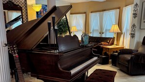 Un pianoforte a coda, una chitarra, uno sgabello imbottito, un divano e una lampada in un soggiorno luminoso con carta da parati decorata e pavimento piastrellato.