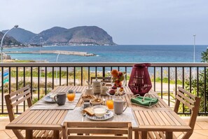 A wooden table with breakfast items, a view of the sea, and a mountainous landscape. - Il Mare in una Stanza | Elegant Sea View Apartment in Mondello (Palermo)