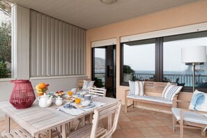 Ein Balkon mit Frühstückstisch, einer roten Vase und Blick auf das Meer.