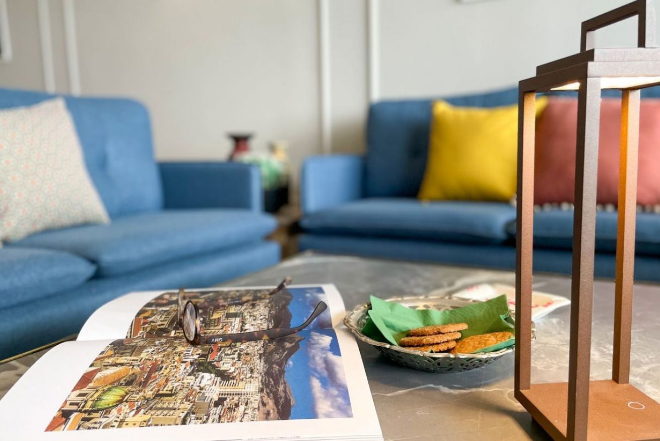 A living room with a sofa, a coffee table with a magazine and snacks, and a decorative wooden stand.