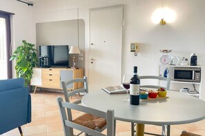 A modern kitchen with a dining table, chairs, a TV, a microwave, and a coffee maker. - Il Mare in una Stanza | Elegant Sea View Apartment in Mondello (Palermo)