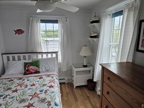Ein Schlafzimmer mit einem Bett, einem Nachttisch, einer Kommode, einem Deckenventilator und einem Fenster mit Vorhängen.