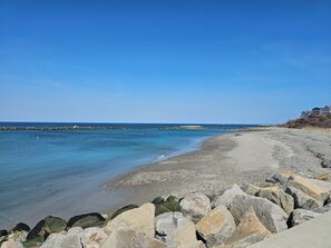 A coastal beach with a rocky shoreline, a clear blue sky, and a large building on the right. - The Beach House, Crescent Beach, Hull (Hull)