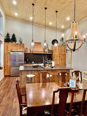 A modern kitchen with wooden cabinets, a stainless steel refrigerator, pendant lights, and a chandelier. - Lodge at Pinhook Gap w/ Sunset Views, Hot tub & EV (Tuckasegee)