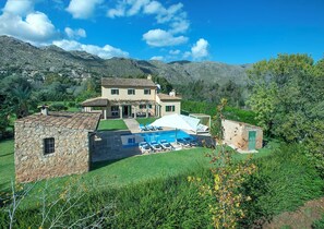 Ein zweistöckiges Haus mit Swimmingpool, ein Steinhaus und Blick auf Berge.