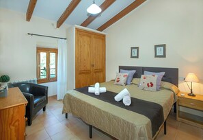 Ein Schlafzimmer mit Bett, Holzschrank, Schreibtisch mit Stuhl, Fenster mit Vorhängen und einer Lampe.