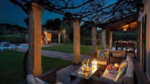 An outdoor patio area with wicker furniture, a glass table, and candles. - Spacious Countryside Villa, A/C Private Pool, Mountain Views in the Desirable Area of La Font! (Pollença)