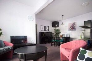 A living room with a flat-screen TV, a round coffee table, a dining area with chairs, and a red armchair.