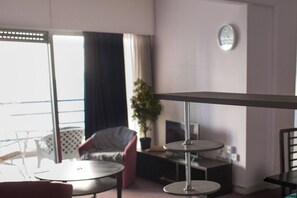 A modern living room with a round table, a red chair, a potted plant, and a large window with curtains.