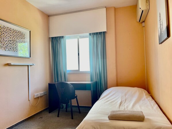 A small hotel room with a single bed, a desk, and a chair.