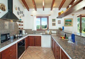 A kitchen with granite countertops, wooden cabinets, a built-in oven, and a window with a view of greenery. - Tranquil Countryside Finca, A/C Private Pool - 15 mins drive from Pollenca, Alcudia & Beaches (Alcudia)