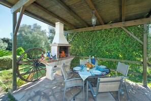 An outdoor patio with a brick oven, a wooden table set for dining, and a vintage wagon wheel. - Tranquil Countryside Finca, A/C Private Pool - 15 mins drive from Pollenca, Alcudia & Beaches (Alcudia)