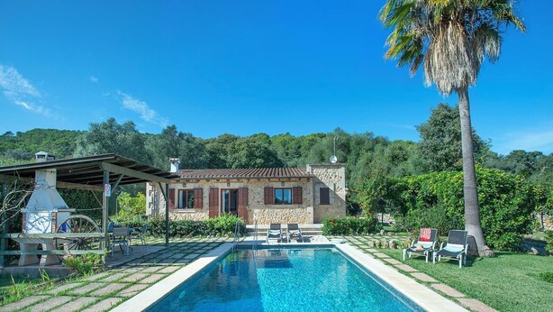 Un área junto a la piscina con un edificio de piedra, mobiliario exterior y una piscina azul cristalina.