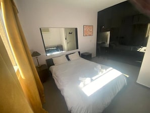Hotellihuone, jossa on sänky, yöpöytä, peili ja ovi, joka johtaa kylpyhuoneeseen.