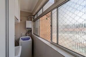 Ein kleines Badezimmer mit Waschmaschine, Waschbecken und einem Fenster mit Metallgitter.