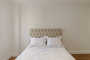 Ein Schlafzimmer mit einer gepolsterten Kopfteile, floralem Bettbezug und Holzboden.