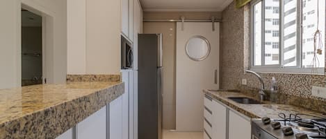 Una cocina con encimeras de granito, electrodomésticos de acero inoxidable y una ventana con vista a edificios.