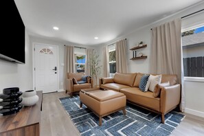 A modern living room with a sofa, armchair, ottoman, and a flat-screen TV. - La Esperanza Unit A Central San Diego Getaway with AC (National City)