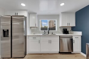 A modern kitchen with white cabinets, stainless steel appliances, a dishwasher, and a window with blinds. - La Esperanza Unit A Central San Diego Getaway with AC (National City)