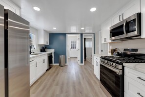 A modern kitchen with white cabinets, stainless steel appliances, and a wooden floor. - La Esperanza Unit A Central San Diego Getaway with AC (National City)