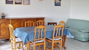 A dining area with a table set for four, wooden chairs, a cabinet, and a sofa. - Oceanfront—Panoramic view and beach access in Ste Cécile (Camiers)