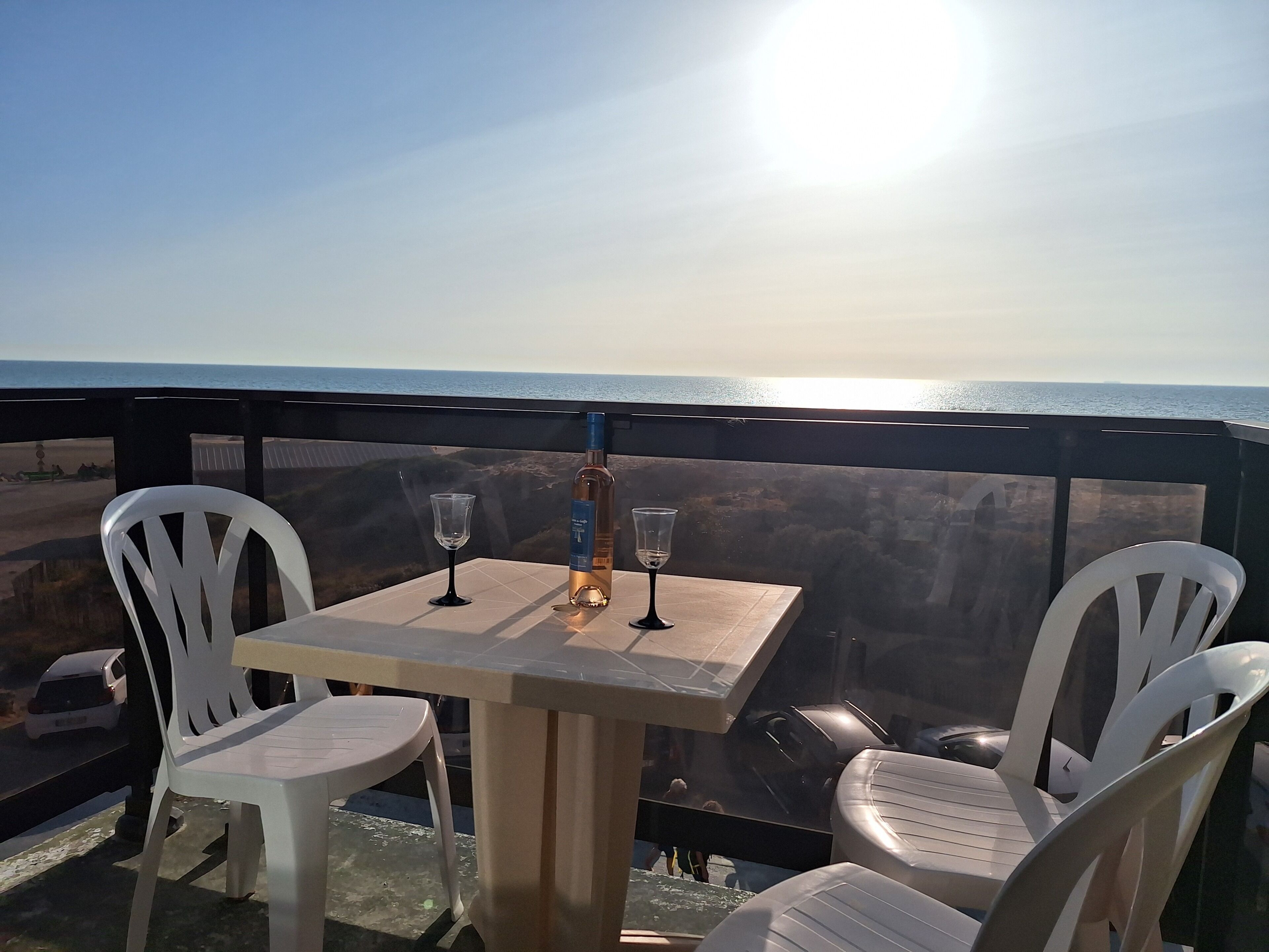 A table with two chairs and a bottle of wine on a balcony overlooking the ocean.
