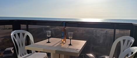 A table with two chairs and a bottle of wine on a balcony overlooking the ocean.