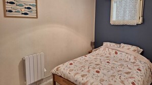A bedroom with a bed, a radiator, a wall-mounted artwork, and a window with patterned curtains. - Oceanfront—Panoramic view and beach access in Ste Cécile (Camiers)