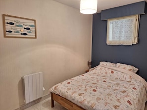 Une chambre à coucher comprenant un lit, un radiateur, une œuvre d’art accrochée au mur et une fenêtre ornée de rideaux à motifs.
