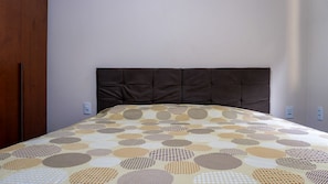 Ein Bett mit einem gemusterten Bettüberwurf, einem dunklen Kopfteil und einer schlichten Wand.