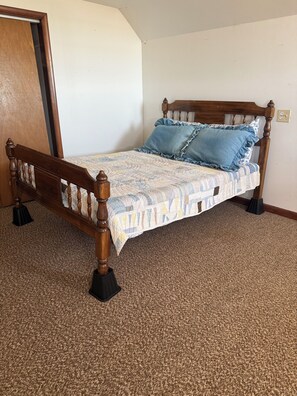A wooden bed with a quilt, two pillows, and a carpeted floor.