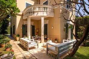 A courtyard with a covered seating area, potted plants, and a building with shutters. - Villa Nunù with private pool (PALERMO)