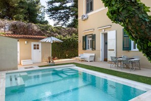 Ein Schwimmbad mit Terrassenbereich, einer weißen Tür und einem kleinen Garten.