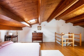 A bedroom with a sloped ceiling, wooden beams, a bed, a dresser, a desk with a lamp, and a small window. - Villa Nunù with private pool (PALERMO)