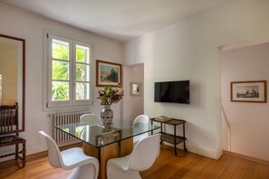 A dining area with a glass table, white chairs, a vase with flowers, and a television on the wall. - Villa Nunù with private pool (PALERMO)